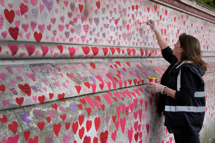 FILE - Volunteer Fran Hall, who lost her husband Steve Mead to COVID-19, re-paints faded hearts on the COVID-19 memorial wall in Westminster in London, Friday, Oct. 15, 2021. (AP Photo/Kirsty Wigglesworth, File)