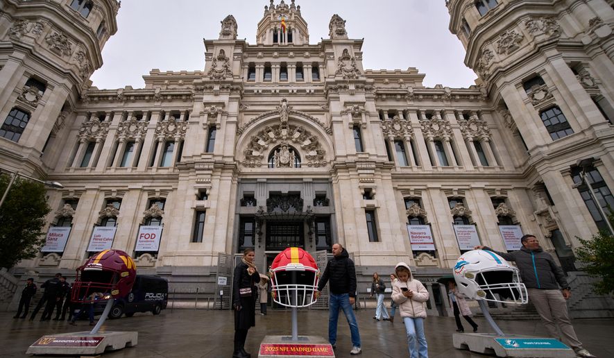 People pose next to giant NFL helmets displayed in front of the Palacio de Cibeles in Madrid, Spain, Thursday, Nov. 13, 2025, ahead of Sunday's NFL football game between the Dolphins and the Commanders. (AP Photo/Manu Fernandez)