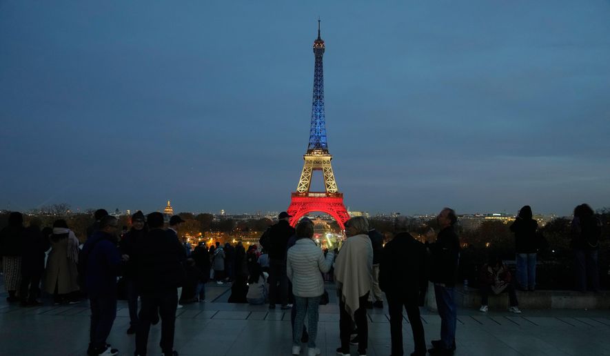 People gather at Trocadero Plaza as the Eiffel Tower is lit in the colors of the French national flag in Paris, Wednesday, Nov. 12, 2025, to honor the victims of the terror attacks at the Bataclan concert hall, cafes, and the national stadium 10 years ago. (AP Photo/Michel Euler)