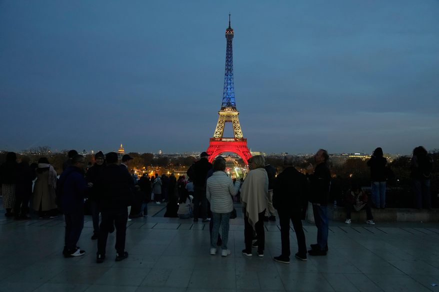People gather at Trocadero Plaza as the Eiffel Tower is lit in the colors of the French national flag in Paris, Wednesday, Nov. 12, 2025, to honor the victims of the terror attacks at the Bataclan concert hall, cafes, and the national stadium 10 years ago. (AP Photo/Michel Euler)