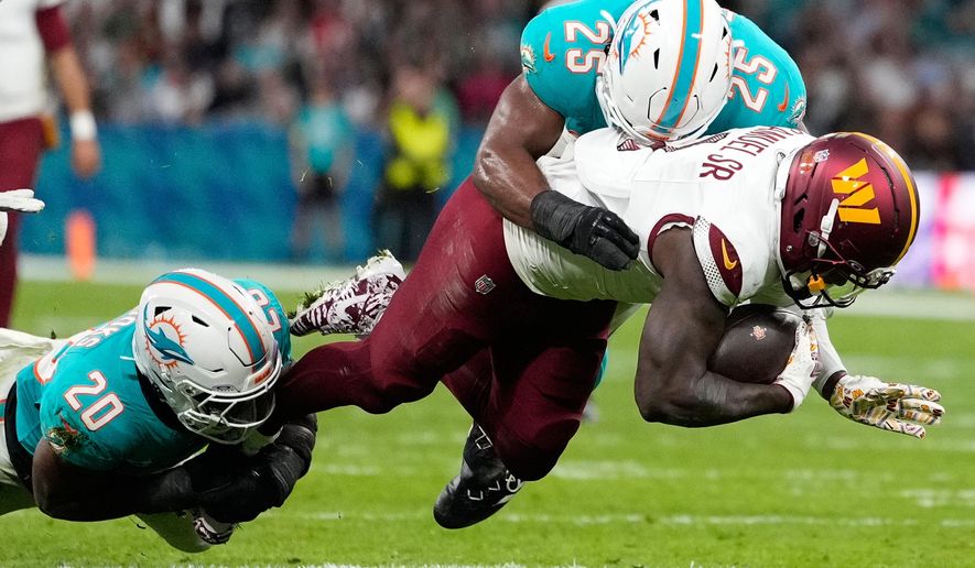 Washington Commanders wide receiver Deebo Samuel (1) is tackled by Miami Dolphins linebacker Jordyn Brooks (20) and linebacker Tyrel Dodson (25) during the first half of an NFL football game between the Washington Commanders and the Miami Dolphins in Madrid, Spain, Sunday, Nov. 16, 2025. (AP Photo/Bernat Armangue)