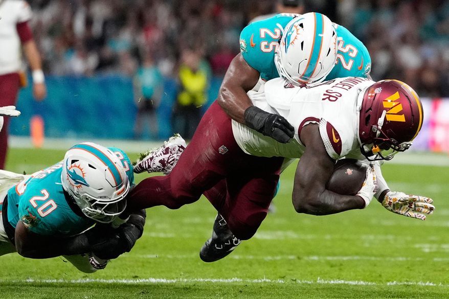 Washington Commanders wide receiver Deebo Samuel (1) is tackled by Miami Dolphins linebacker Jordyn Brooks (20) and linebacker Tyrel Dodson (25) during the first half of an NFL football game between the Washington Commanders and the Miami Dolphins in Madrid, Spain, Sunday, Nov. 16, 2025. (AP Photo/Bernat Armangue)