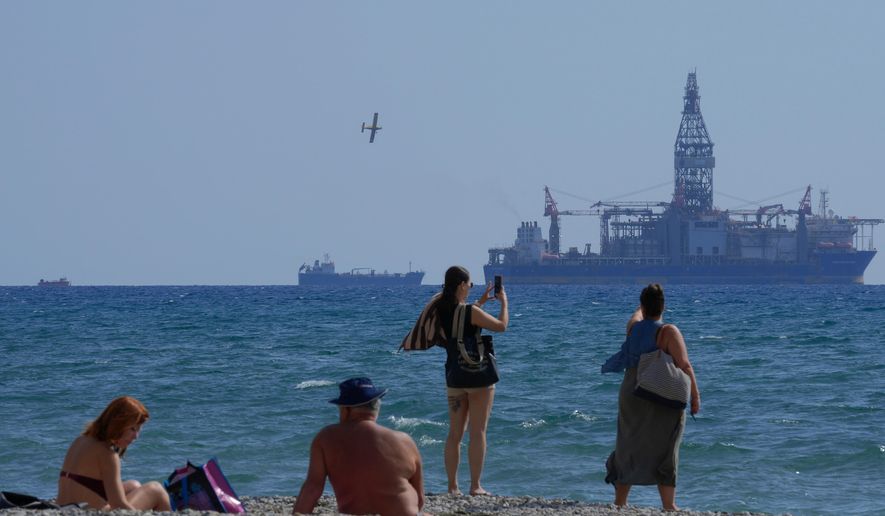 FILE - People on the beach take photos of the 'Tungsten Explorer' drilling ship, in the southern coastal city of Larnaca, Cyprus, Wednesday, Nov. 3, 2021. (AP Photo/Petros Karadjias, File)