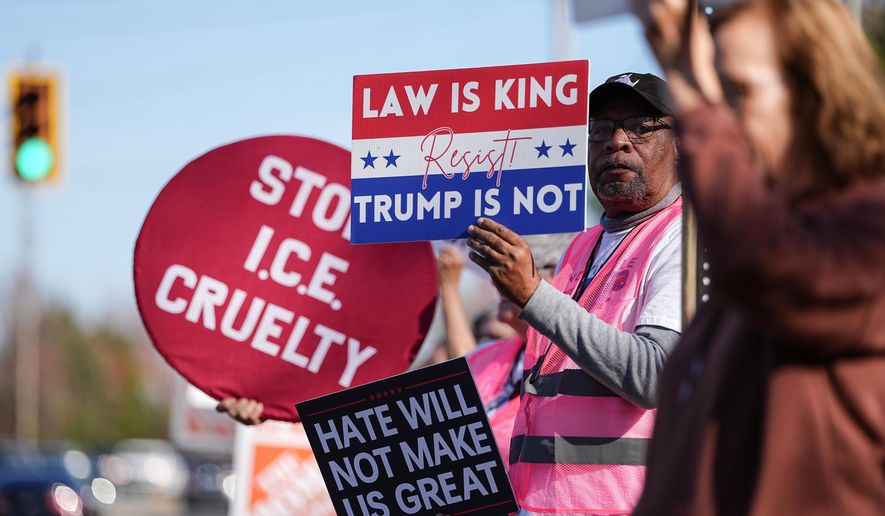 Protesters hold signs during the arrival of federal law enforcement, Wednesday, Nov. 19, 2025, in Charlotte, N.C. (AP Photo/Matt Kelley)