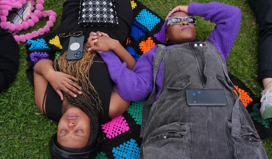 Participants hold hands as they lie on the ground during a gender-based violence protest at the forecourt of the botanical gardens in Johannesburg, South Africa, Friday, Nov. 21, 2025. (Misper Apawu)