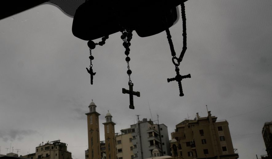 Rosaries and crosses hang from a car's rearview mirror as buildings and church towers rise in the background in Beirut, Lebanon, Friday, Nov. 14, 2025. (AP Photo/Hassan Ammar)