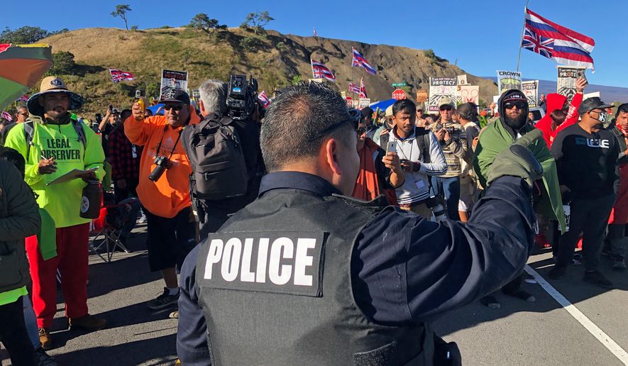 A police officer gestures at demonstrators blocking a road at the base of Hawaii's tallest mountain, Monday, July 15, 2019, in Mauna Kea, Hawaii, who are protesting the construction of a giant telescope on land that some Native Hawaiians consider sacred. (AP Photo/Caleb Jones)
