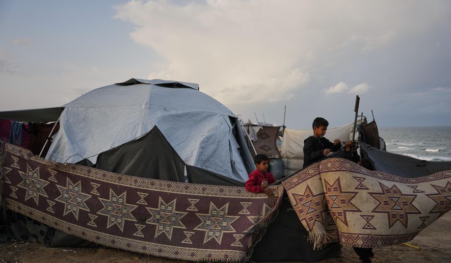 Fahd Al-Madhoun, 10, and his 7-year-old brother, Ziad, work to repair their family's tent after it was damaged by a storm at a temporary camp for displaced Palestinians on the beach in Deir al-Balah, in central Gaza, Tuesday, Nov. 25, 2025. (AP Photo/Abdel Kareem Hana)