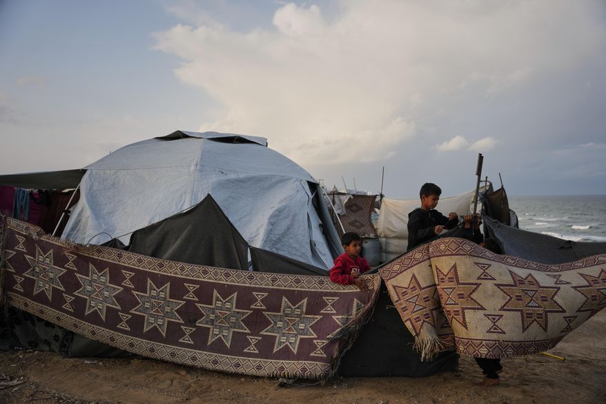 Fahd Al-Madhoun, 10, and his 7-year-old brother, Ziad, work to repair their family's tent after it was damaged by a storm at a temporary camp for displaced Palestinians on the beach in Deir al-Balah, in central Gaza, Tuesday, Nov. 25, 2025. (AP Photo/Abdel Kareem Hana)
