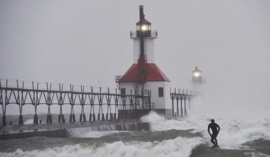 A surfer rides through blowing snow as Lake Michigan waves crash into the St. Joseph Inner and Outer Lighthouses Wednesday, Nov. 26, 2025, in St. Joseph, Mich. (Don Campbell/The Herald-Palladium via AP)