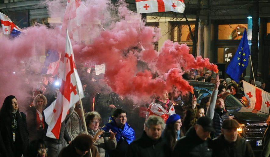 Demonstrators with Georgian and EU flags light flares as they gather in the Georgian capital of Tbilisi, on Friday, Nov. 28, 2025, to mark 365 days of non-stop protests against the government's decision to halt talks on joining the European Union. (AP Photo/Zurab Tsertsvadze)