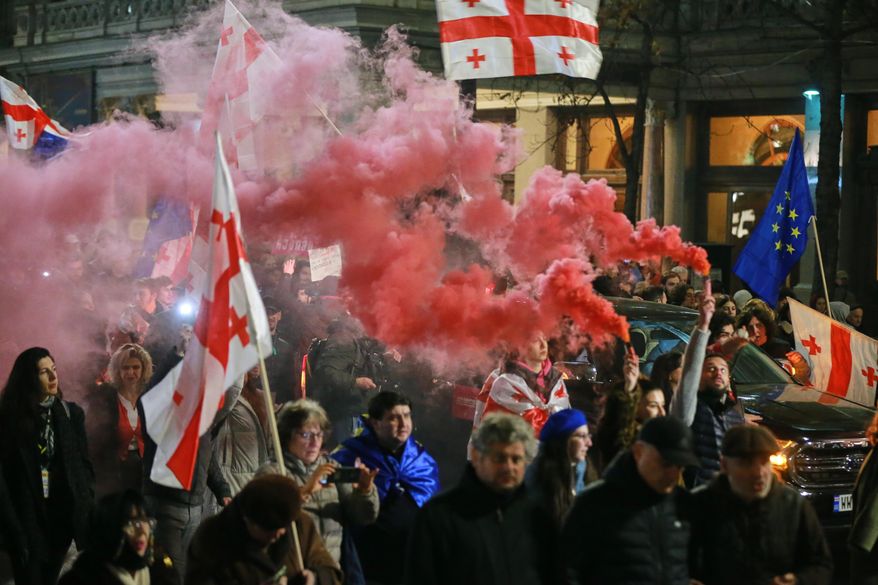 Demonstrators with Georgian and EU flags light flares as they gather in the Georgian capital of Tbilisi, on Friday, Nov. 28, 2025, to mark 365 days of non-stop protests against the government's decision to halt talks on joining the European Union. (AP Photo/Zurab Tsertsvadze)