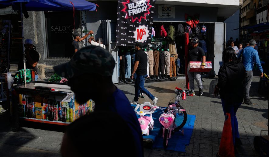 Pedestrians walk past a storefront promoting Black Friday discounts in Caracas, Venezuela, Friday, Nov. 28, 2025. (AP Photo/Ariana Cubillos)