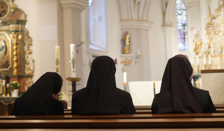 Three Christian nuns, seen from behind, looking at the church altar in traditional black clothes. File photo credit: Julija Ogrodowski via Shutterstock.