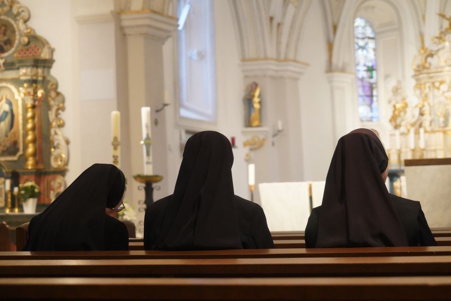Three Christian nuns, seen from behind, looking at the church altar in traditional black clothes. File photo credit: Julija Ogrodowski via Shutterstock.
