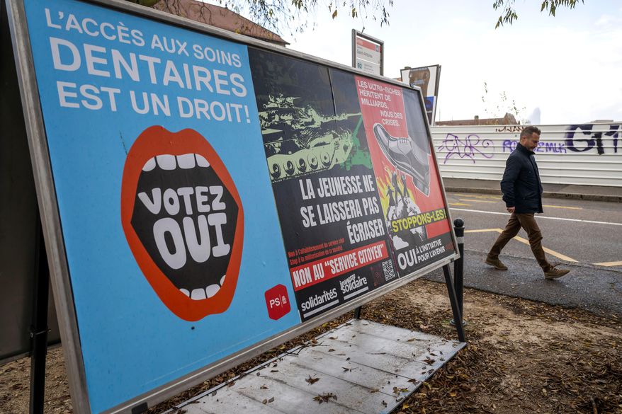 A person walks past referendum posters of political parties and associations as Swiss voters are casting ballots to decide whether women, like men, must do national service in the military, civil protection teams or in other forms, in Geneva, Switzerland, on Nov. 26, 2025. (Martial Trezzini/Keystone via AP)