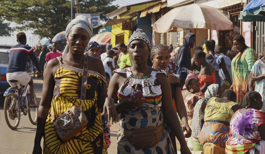Women walk past people shopping at a market in Bissau, Guinea-Bissau, Friday, Nov. 28, 2025. (AP Photo/Darcicio Barbosa)