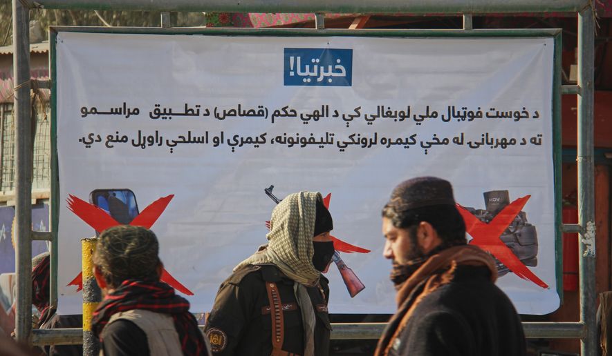 A Taliban policeman, center, and two other men walk past a poster stating that cameras, phones, and weapons are banned inside a stadium where a public execution was taking place in the city of Khost, eastern Afghanistan, Tuesday, Dec. 2, 2025. (AP Photo/Saifullah Zahir)