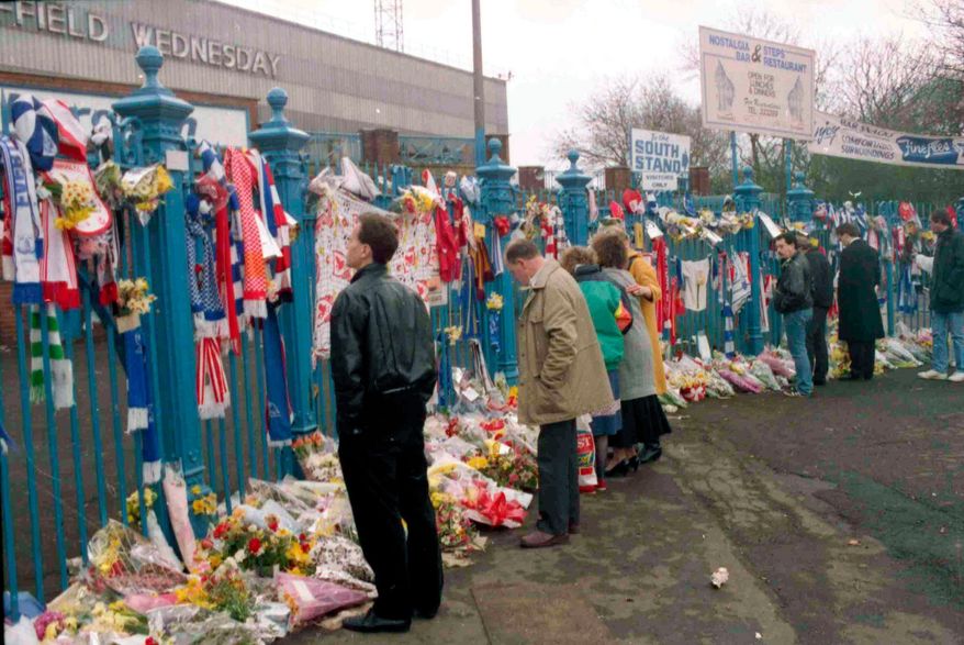 FILE- In this file photo dated April 17, 1989, soccer fans arrive to pay their respects and look at the flowers, scarves and banners, left on the gates at Hillsborough Football Stadium. (AP Photo/ Peter Kemp, File)