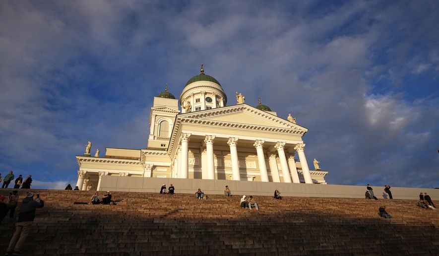People enjoy the sunny weather with the Helsinki Cathedral of the background in Helsinki, Finland, Friday, Nov. 14, 2025. (AP Photo/Sergei Grits)