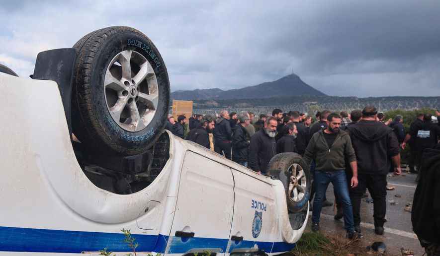 Farmers gather next to an overturned police vehicle during clashes with officers blocking their march to Chania's airport on Crete, Greece, Monday, Dec. 8, 2025, amid protests over delayed EU farm subsidies. (AP Photo/Giannis Angelakis)