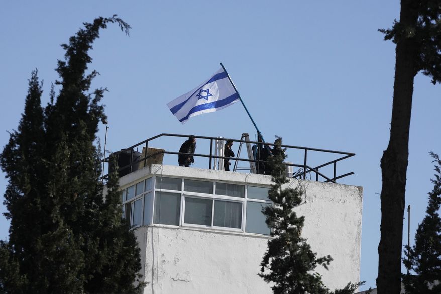 Israeli police and officials hang an Israeli flag on the compound of the United Nations agency for Palestinian refugees in East Jerusalem, after Israel police forcibly entered the compound, Monday, Dec. 8, 2025. (AP Photo/Mahmoud Illean)