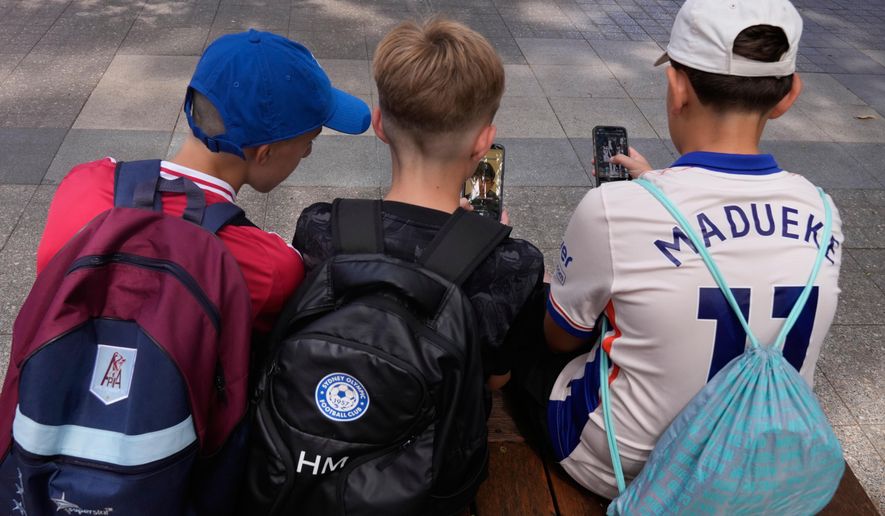 Hugo Winwood-Smith, right, Hardy Macpherson and Edan Abou, left, all 11-years-old, use their phones while sitting outside a school in Sydney, Monday, Dec. 8, 2025. (AP Photo/Rick Rycroft)