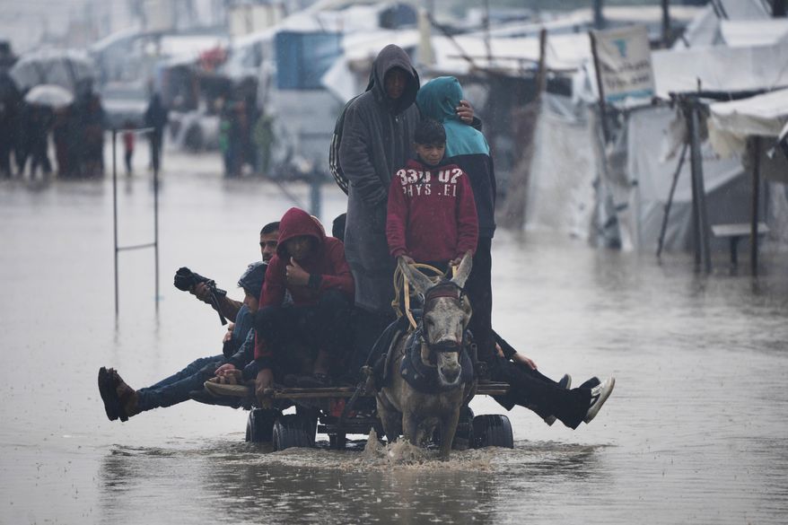 Palestinians cross a flooded street following heavy rain in Khan Younis, southern Gaza Strip, Thursday, Dec. 11, 2025. (AP Photo/Abdel Kareem Hana)