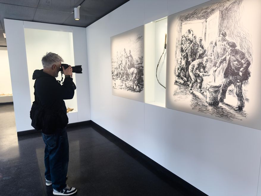 A photojournalist takes photos of sketches made by survivors after their liberation from Auschwitz and displayed near a whip, used in the Camp, in its new permanent exhibition at the former Nazi Death Camp Auschwitz in Oswiecim, Poland, Thursday, Dec. 11, 2025. (AP Photo/Rafal Niedzielski)