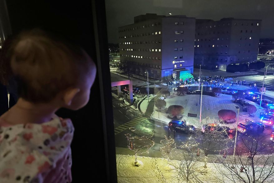 A hospitalized child looks out the window at volunteers who are shining lights up into the pediatric wing of Corewell Health Children's during a Moonbeams for Sweet Dreams event Wednesday, Dec. 10, 2025, in Royal Oak, Mich. (AP Photo/Mike Householder)