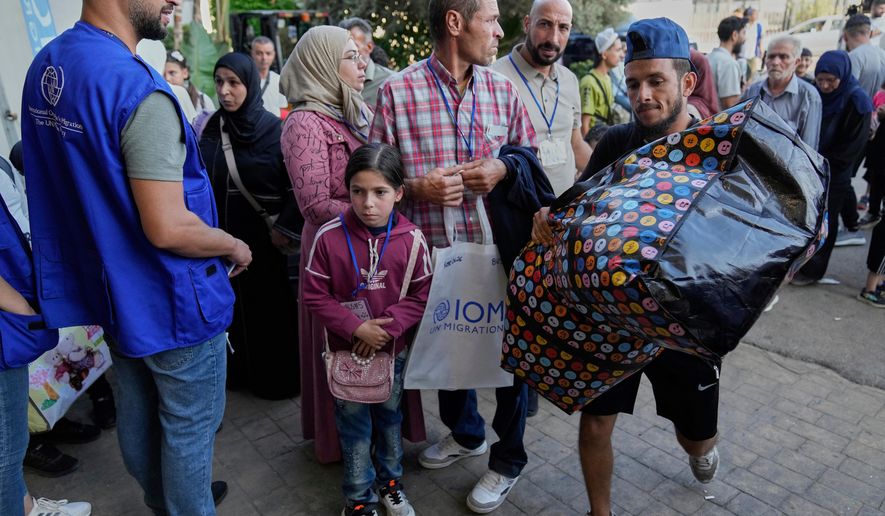 A worker, right, carries a bag as Syrian refugees line up at a gathering point to be checked by Lebanese security forces before they board buses to return home to Syria, in Beirut, Lebanon, Thursday, Sept. 11, 2025. (AP Photo/Hussein Malla, File)