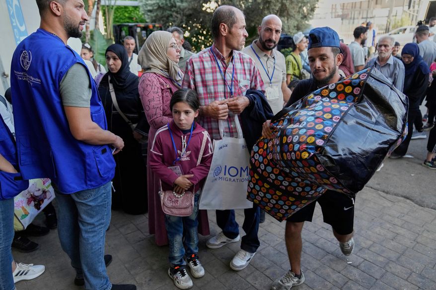 A worker, right, carries a bag as Syrian refugees line up at a gathering point to be checked by Lebanese security forces before they board buses to return home to Syria, in Beirut, Lebanon, Thursday, Sept. 11, 2025. (AP Photo/Hussein Malla, File)