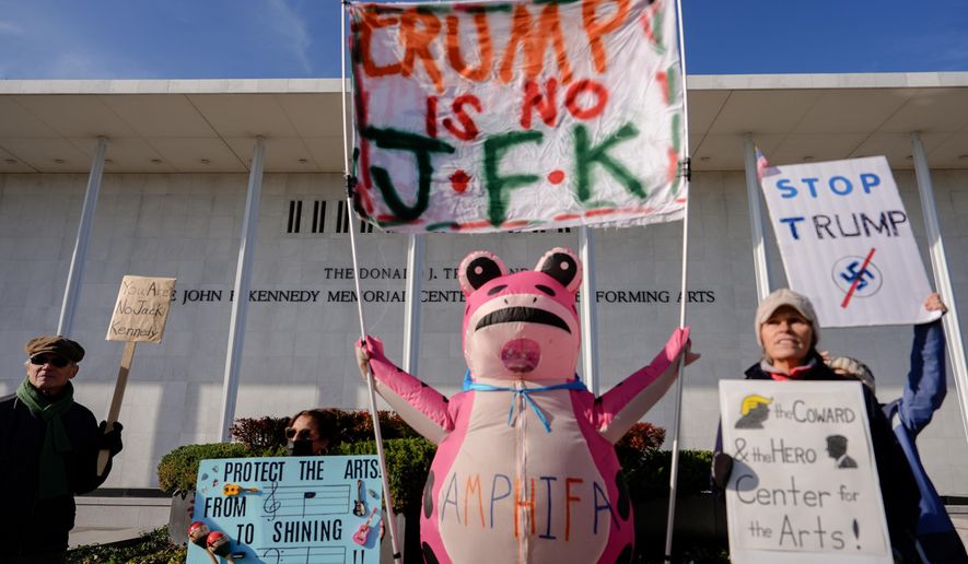Demonstrators, including Nadine Siler, of Waldorf, Md., dressed in a pink frog costume, hold up signs at a designated protest point in front of the John F. Kennedy Memorial Center for the Performing Arts, a day after a Trump-appointed board voted to add President Donald Trump's name to the Kennedy Center, Saturday, Dec. 20, 2025, in Washington. (AP Photo/Julia Demaree Nikhinson)