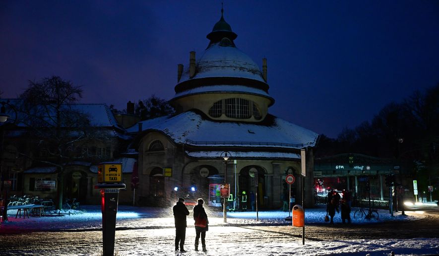 Passers-by stand in the light of a fire department help point in Berlin, Germany, Saturday, Jan. 3, 2025, during a power cut in south-west Berlin after a fire on a cable bridge. (Christoph Gollnow/dpa via AP)