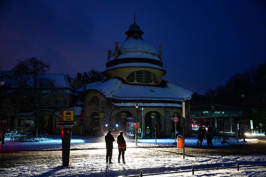 Passers-by stand in the light of a fire department help point in Berlin, Germany, Saturday, Jan. 3, 2025, during a power cut in south-west Berlin after a fire on a cable bridge. (Christoph Gollnow/dpa via AP)