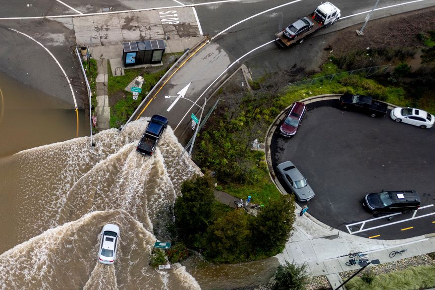 Vehicles drive on a flooded road during a king tide event in Corte Madera, Calif., Saturday, Jan. 3, 2026. (Stephan Lam/San Francisco Chronicle via AP)