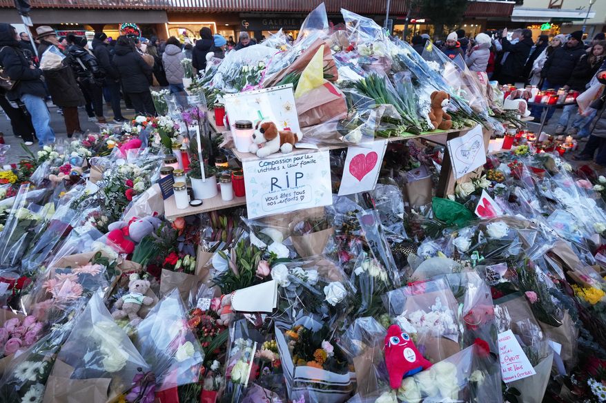 People stand around floral tributes and candles placed outside the sealed off Le Constellation bar in Crans-Montana, Swiss Alps, Switzerland, Saturday, Jan. 3, 2026, where a devastating fire left dead and injured during the New Year's celebrations. (AP Photo/ Antonio Calanni)