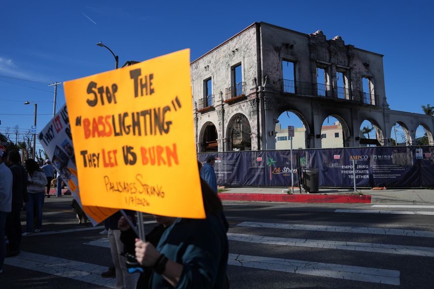 Demonstrators hold signs in front of a fire-ravaged building on the one-year anniversary of the Palisades Fire in the Pacific Palisades neighborhood of Los Angeles Wednesday, Jan. 7, 2026. (AP Photo/Jae C. Hong)