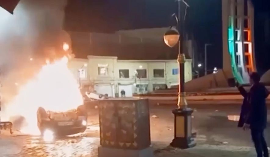 This frame grab from a video released Friday, Jan. 9, 2026, by Iranian state television shows a man holding a device to document burning vehicles during a night of mass protests in Zanjan, Iran. (Iranian state TV via AP)