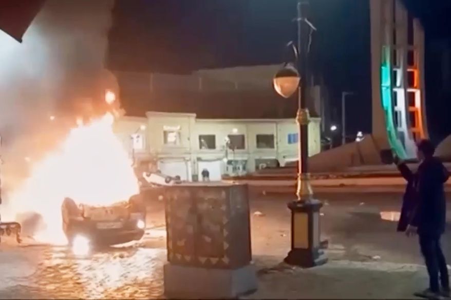 This frame grab from a video released Friday, Jan. 9, 2026, by Iranian state television shows a man holding a device to document burning vehicles during a night of mass protests in Zanjan, Iran. (Iranian state TV via AP)