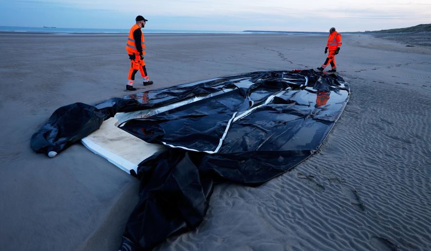 Town employees walk next to an inflatable boat punctured by French police and used by migrants to cross the Channel, Monday, Dec. 22, 2025 on the beach of Gravelines, northern France. (AP Photo/Jean-Francois Badias, File)