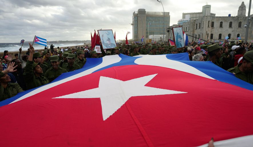 People carry a Cuban flag during a government-organized rally protesting the killing of Cuban officers in Venezuela while U.S. forces captured Venezuelan President Nicolas Maduro and his wife, in Havana, Cuba, Friday, Jan. 16, 2026. (AP Photo/Ramon Espinosa)