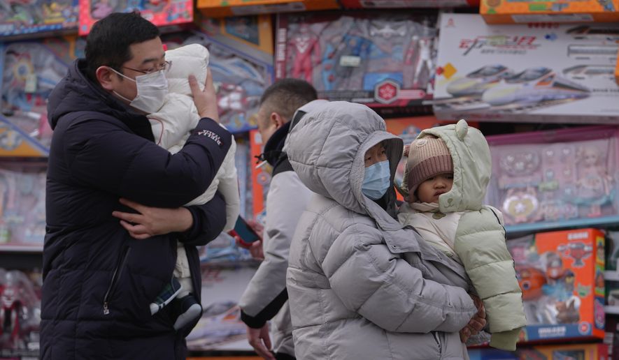 People carry their toddlers by a toy store in Beijing, Monday, Jan. 19, 2026. (AP Photo/Andy Wong)