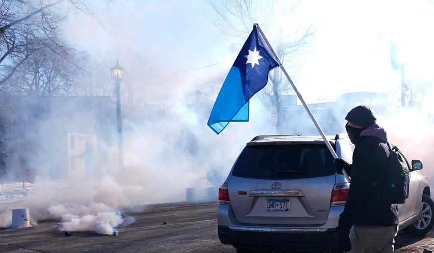 A person holds a Minnesota state flag as federal immigration officers deploy tear gas Saturday, Jan. 24, 2026, in Minneapolis. (AP Photo/Abbie Parr)