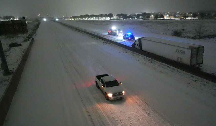 A pickup moves westbound on Interstate-20 as tow trucks, back, prepare to pull a disabled tractor trailer on the eastbound lanes during a snowstorm early Sunday, Jan. 25, 2026, in Arlington, Texas. (AP Photo/Julio Cortez)