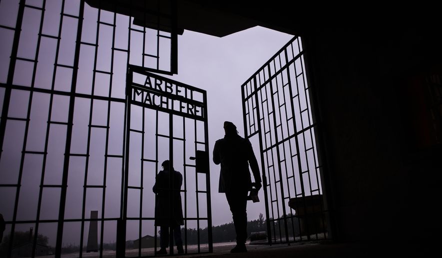 Two men enter the Nazi Concentration Camp Sachsenhausen through a gate with writing "Arbeit macht frei" in German reading "Work makes free", on the eve on the International Holocaust Memorial Day in Oranienburg, Germany, Monday, Jan. 26, 2026. (AP Photo/Markus Schreiber)