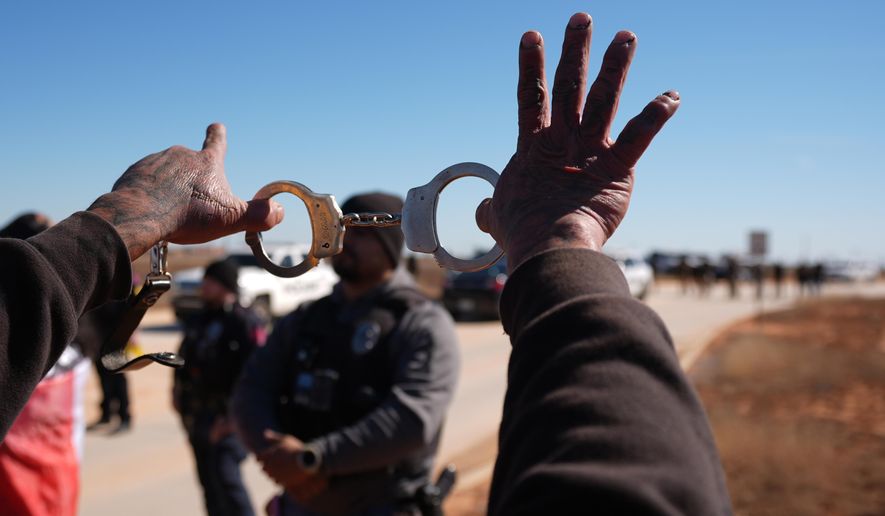 A protester holds up handcuffs to taunt a police officer during a demonstration outside the South Texas Family Residential Center detention facility where Liam Ramos and his father are being detained in Dilley, Texas, Wednesday, Jan. 28, 2026. (AP Photo/Eric Gay)
