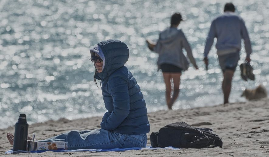 A bundled up Lucia Amato, of Argentina, sits on the shore while waiting for a friend in Miami Beach, Fla., Thursday, Jan. 29, 2026.A bundled up (AP Photo/Marta Lavandier)