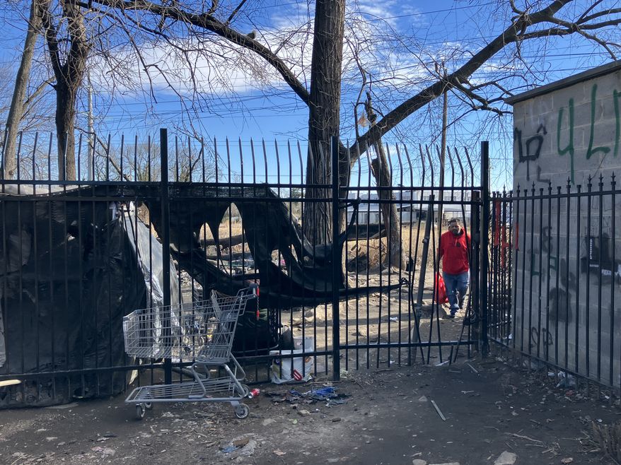 Unidentified people shuffle into the Marylander Condominiums through a gap in the security fence on Monday, Jan. 12. Property managers say unknown vagrants created the opening when workers installed the fence last year. (Sean Salai/The Washington Times)