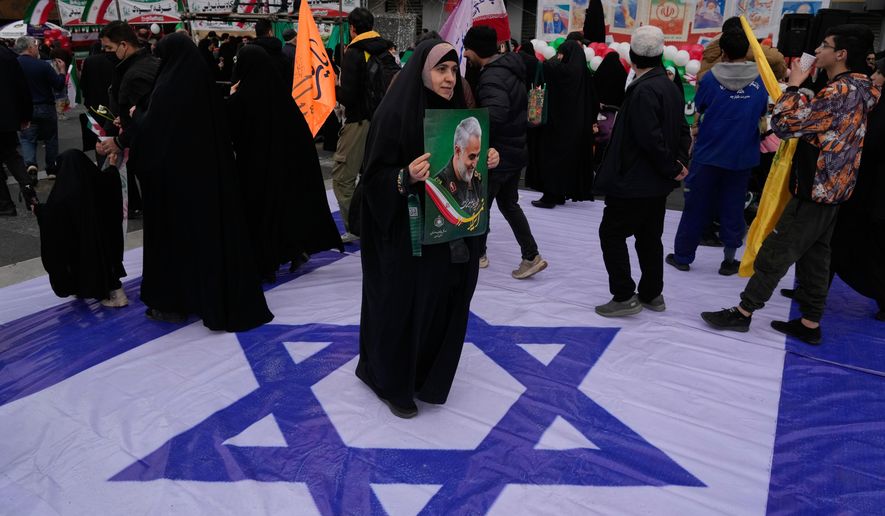 A woman holds a poster of the late commander of Iran's Revolutionary Guard expeditionary Quds Force, Gen. Qassem Soleimani, who was killed in a U.S. drone attack in 2020 in Iraq, as she stands on a banner containing an image of the Israeli flag in an annual rally marking 1979 Islamic Revolution at the Azadi, or Freedom, Street in Tehran, Iran, Wednesday, Feb. 11, 2026. (AP Photo/Vahid Salemi)